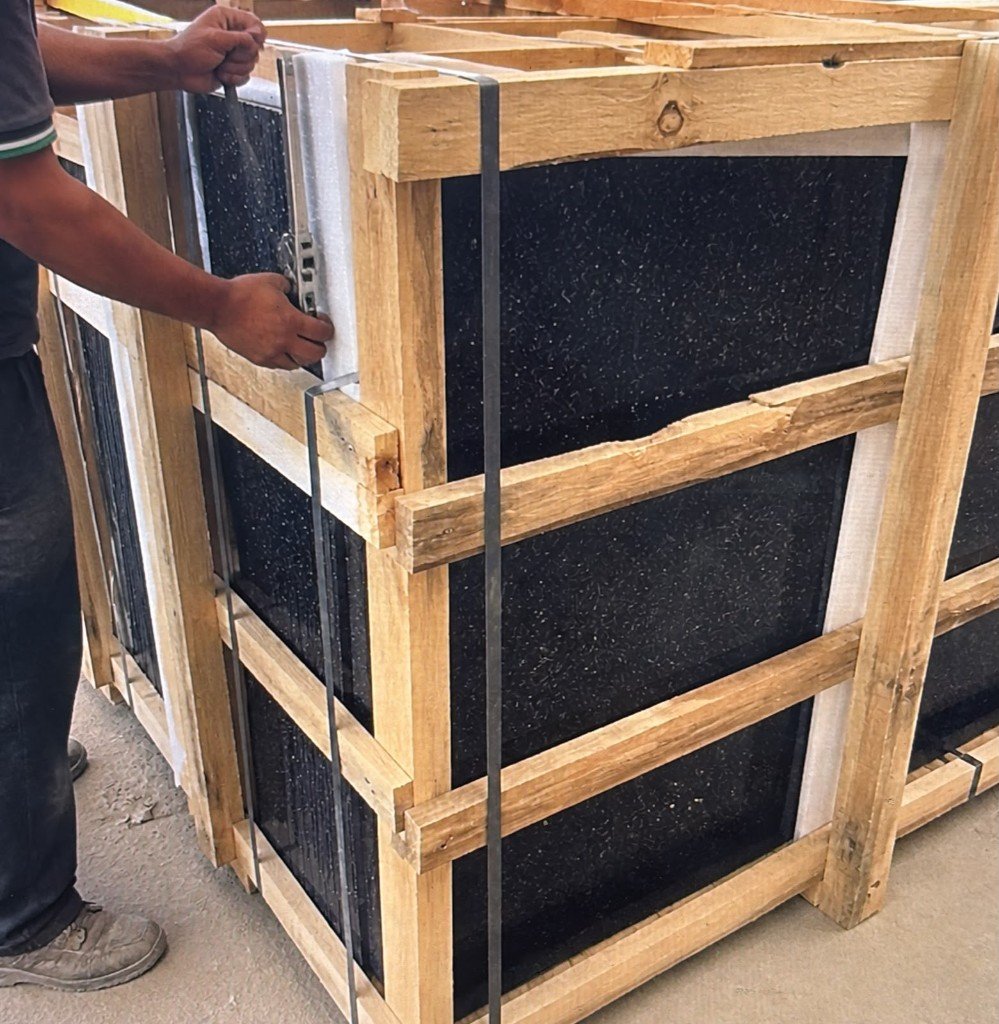 Worker tensioning metal straps on Black Galaxy granite crate before container loading